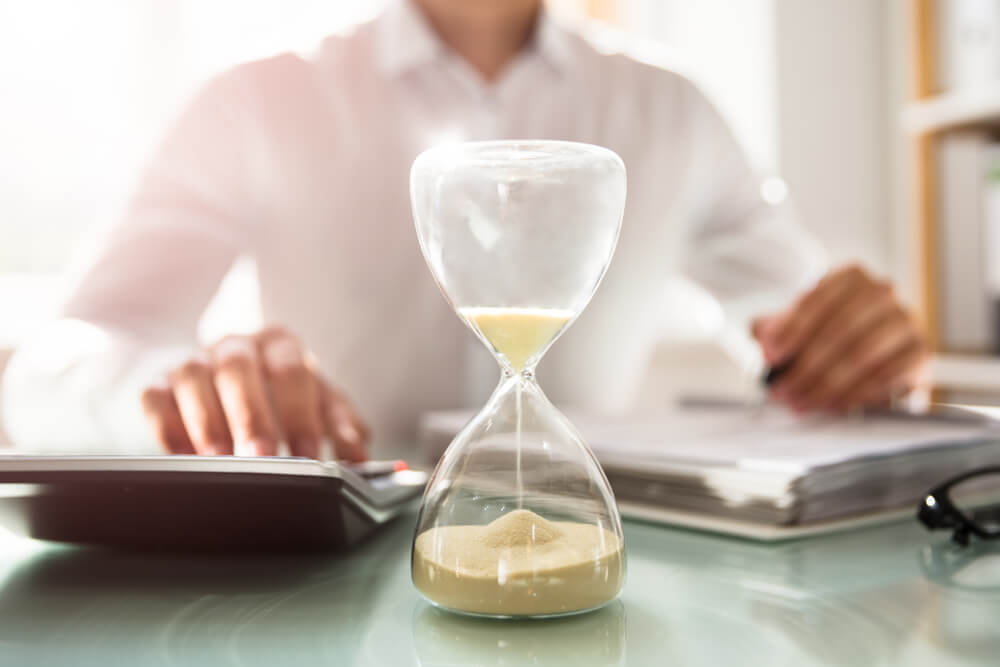 Klepsydra symbolizująca uciekający czas, w tle mężczyzna analizujący dane finansowe – medifaktor.pl