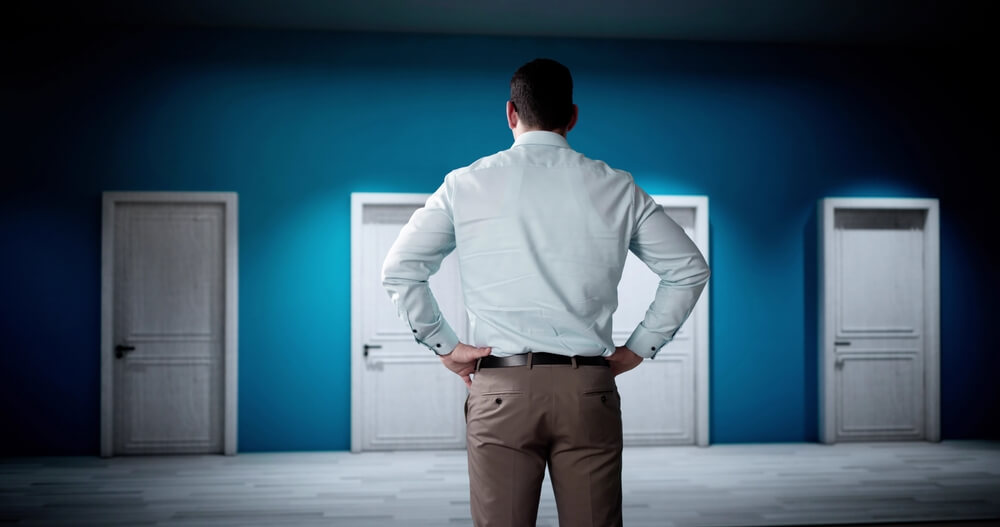 Mężczyzna stojący przed czterema parami drzwi – wybór ścieżki biznesowej – medifaktor.pl